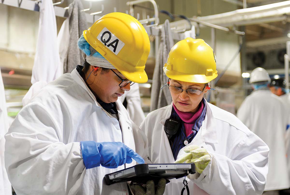 Two manufactures in protective gear looking at an ipad.